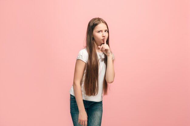 Secret, gossip concept. Young teen girl whispering a secret behind her hand isolated on trendy pink studio.