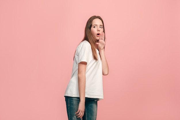 Secret, gossip concept. Young teen girl whispering a secret behind her hand isolated on trendy pink