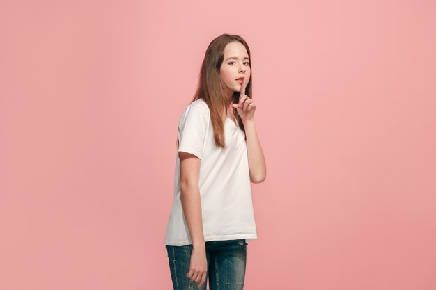 Secret, gossip concept. Young teen girl whispering a secret behind her hand isolated on trendy pink