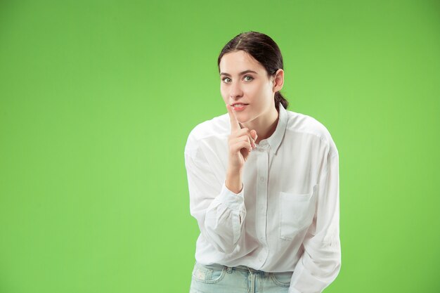 Secret, gossip concept. Young woman whispering a secret behind her hand. Business woman isolated on trendy green studio background. Young emotional woman. Human emotions, facial expression concept.