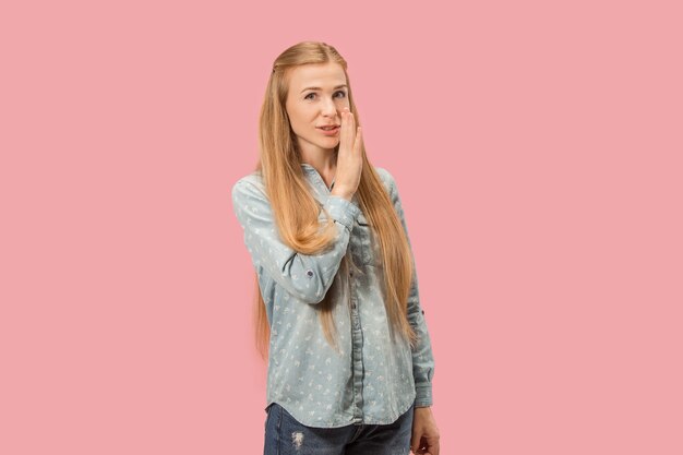 Secret, gossip concept. Young woman whispering a secret behind her hand. Business woman isolated on trendy pink studio background. Young emotional woman. Human emotions, facial expression concept.