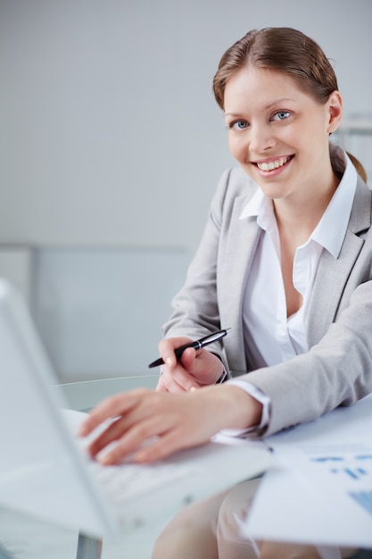 Secretary typing on the laptop and holding a pen