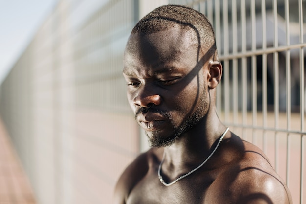 Seductive African American man with muscels poses with naked chest before the fence