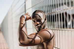 Бесплатное фото Соблазнительный афроамериканец с мускулами позирует с обнаженным сундуком перед забором