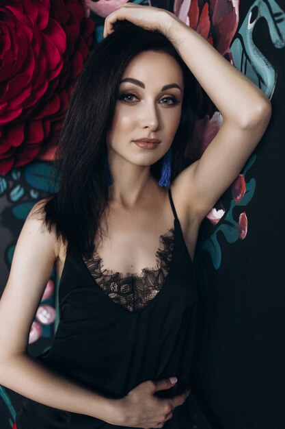 Seductive woman in black lingerie poses before large colorful flowers