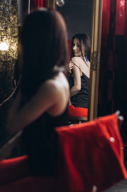 魅惑的な女性は鏡の前に座って彼女の服を脱ぐ