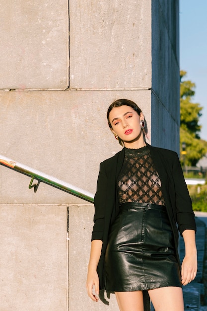 Seductive young woman in black fashionable clothes in front of wall