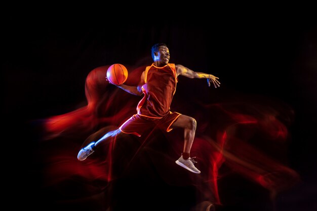 See the target. African-american young basketball player of red team in action and neon lights over dark studio background. Concept of sport, movement, energy and dynamic, healthy lifestyle.