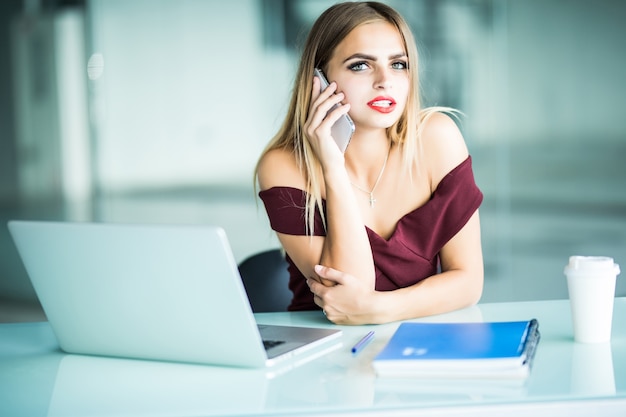 Free photo see you tomorrow. cheerful young beautiful woman in glasses talking on the phone and using laptop with smile while sitting at her working place