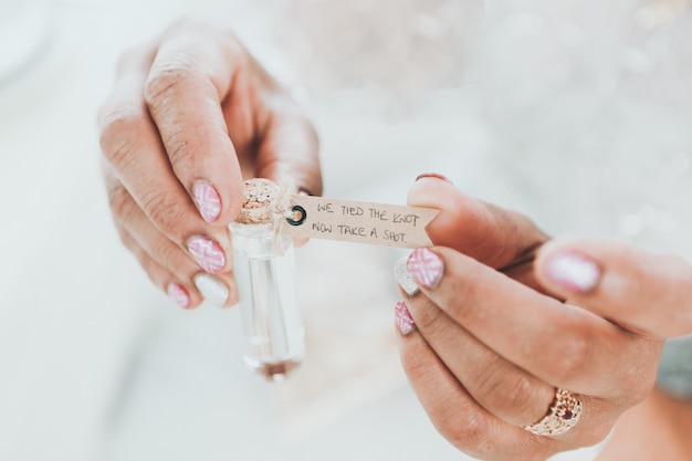 Free photo selective closeup shot of a female holding a small glass bottle with words written on a tag