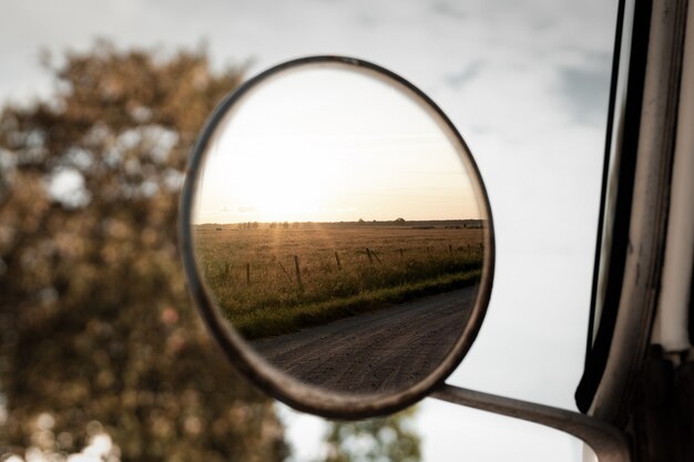 Selective focus closeup shot of the view of a grass field in the round side mirror of a vehicle