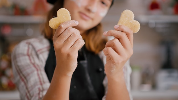 Foto gratuita messa a fuoco selettiva del nipote che tiene l'impasto per biscotti a forma di cuore nelle mani