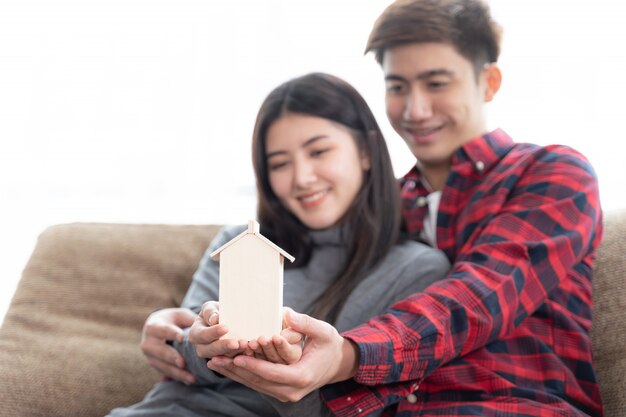 Selective focus at hand's young couple holding mini wooden house on the sofa in bedroom