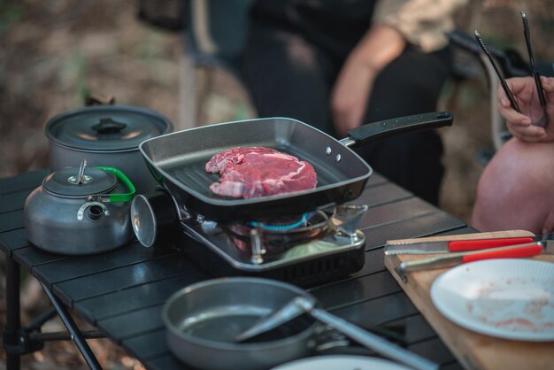 Selective focus hand of young asian woman cooking and her friend enjoy to make the meal in pan They are talk and laugh with fun together while camping in nature park