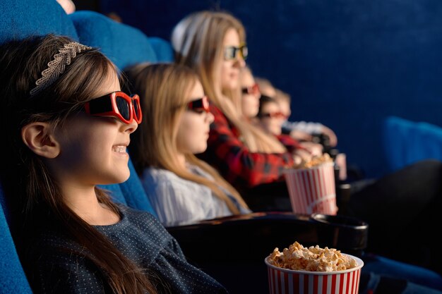 3 dメガネをかけている子供を笑い、ポップコーンを食べ、面白い映画を見ている選択的な焦点。映画館で友達との時間を楽しんでいるかわいい女の子