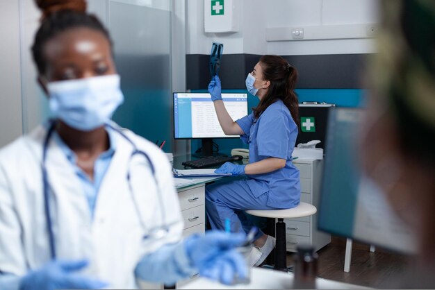 Selective focus on medical nurse analyzing lungs radiography during clinical examination in hospital office. African american with face mask against coronavirus explaining disease symptoms