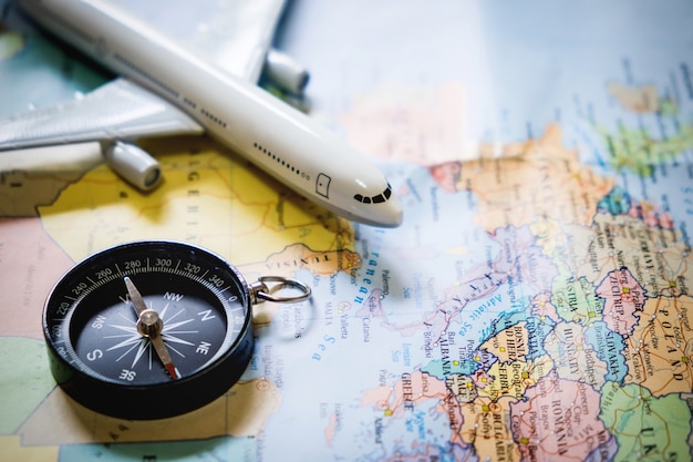 Селективный фокус миниатюрного туриста на компасе над картой с пластиковым игрушечным самолетом, абстрактным фоном для концепции путешествия.