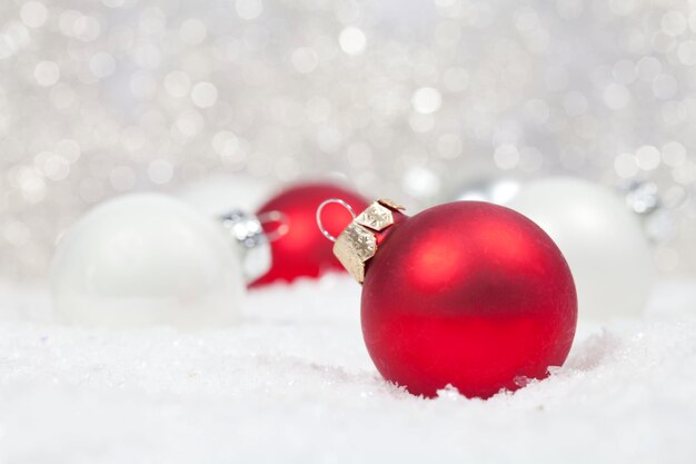 Selective focus of red and white Christmas bulbs in the snow with bokeh lights on the background