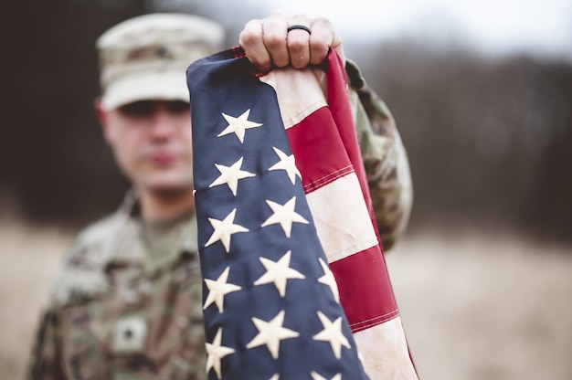 Selective focus shot of an American soldier holding the American flag close to the camera