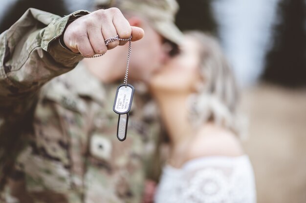 Selective focus shot of an American soldier holding his dog tag while kissing his lovely wife