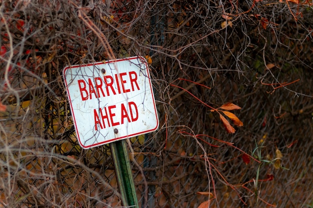 Selective focus shot of a barrier ahead sign leaned against a metal fence