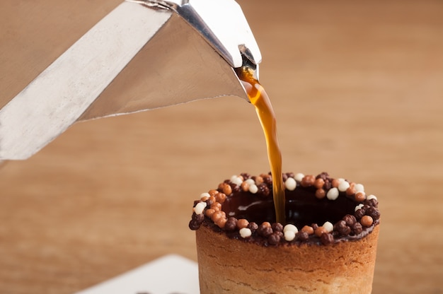 Selective focus shot of coffee pouring in a biscuit cup on a wooden surface