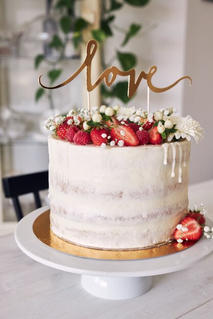 붉은 열매, 꽃, 케이크 토퍼와 함께 맛있는 하얀 웨딩 케이크의 선택적 초점 샷
