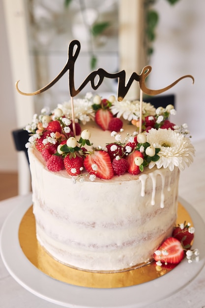 Selective focus shot of delicious white wedding cake with red berries, flowers and cake topper