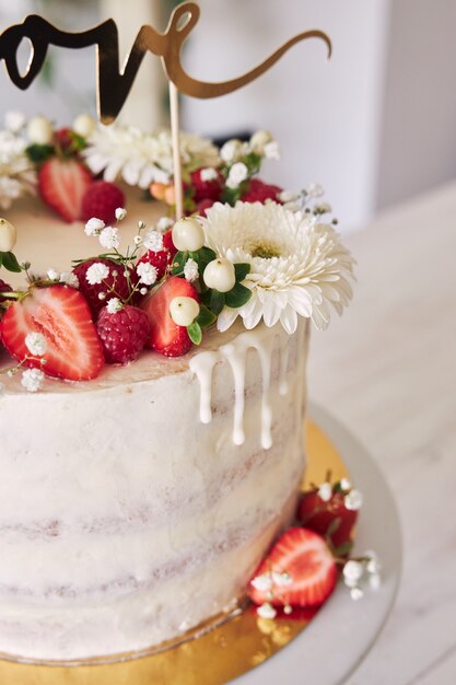 Selective focus shot of delicious white wedding cake with red berries, flowers and cake topper