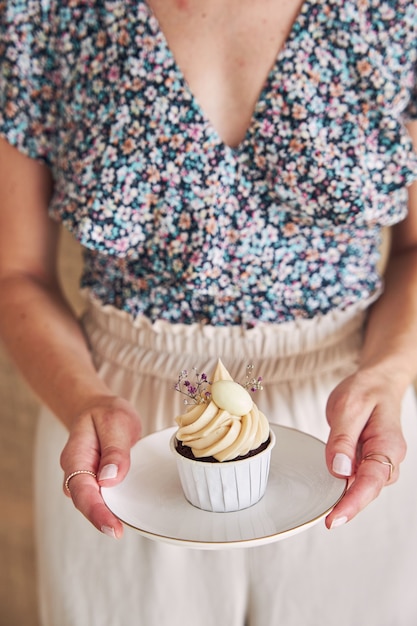 ホワイトクリームのトッピングでおいしいチョコレートカップケーキを保持している女性の選択的なフォーカスショット