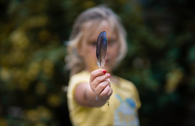 Selective focus shot of a girl holding a colorful feather in a field