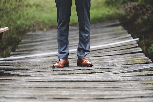 Selective focus shot of the grooms lower body wearing a tuxedo pants and brown shoes