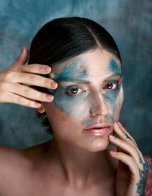 Foto gratuita messa a fuoco selettiva di una ragazza italiana con vernice turchese sul viso e un tatuaggio sulla mano