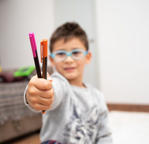 Selective focus shot of a little boy with glasses showing the colorful markers