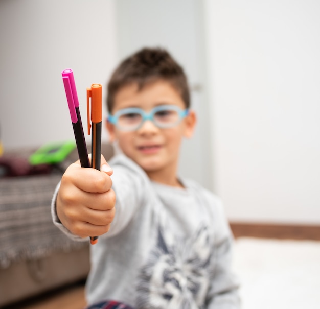 다채로운 마커를 보여주는 안경을 쓴 어린 소년의 선택적 초점
