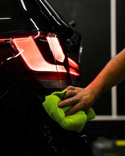 Selective focus shot of a man cleaning car's back headlight with a microfiber cloth