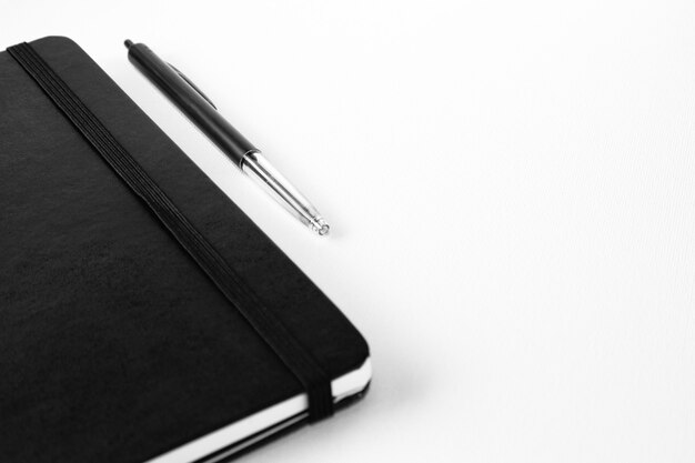 Selective focus shot of a pen near a notebook on a white surface
