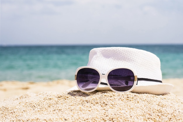 Selective focus shot of sunglasses and a white hat on a sandy beach