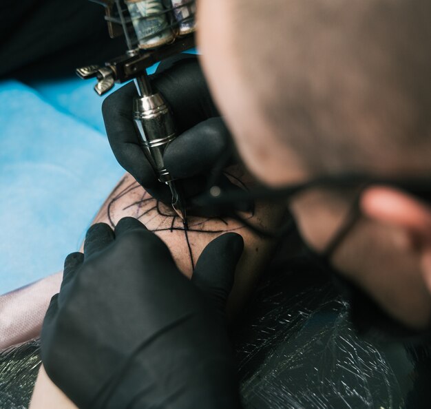 Selective focus shot of a tattoo artist with black gloves creating a tattoo on a man's arm