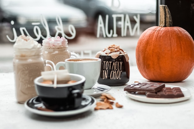 Selective focus shot of a variety of hot drinks, chocolate bars, and a pumpkin on the table