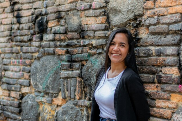 Selective focus shot of a young happy Colombian female leaning against a brick wall