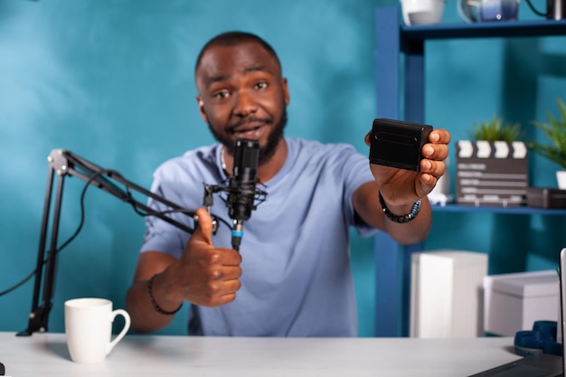 Selective focus on social media influencer giving positive feedback after review of npf rechargeable battery pack sitting at desk. Content creator reviewing lithium ion accumulator in vlogging studio.