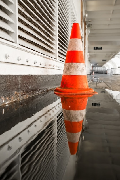 Selective shot of an orange traffic cone on the side of the hallway with a puddle reflecting it