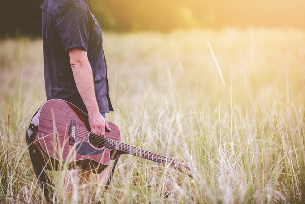 Выборочный снимок человека, держащего коричневую акустическую гитару, стоящего посреди поля травы
