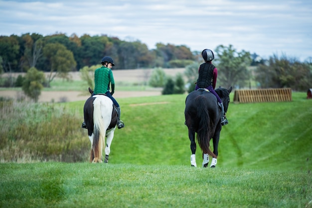 Selective shot of two people wearing horse riding vests riding on horses with black and white tails