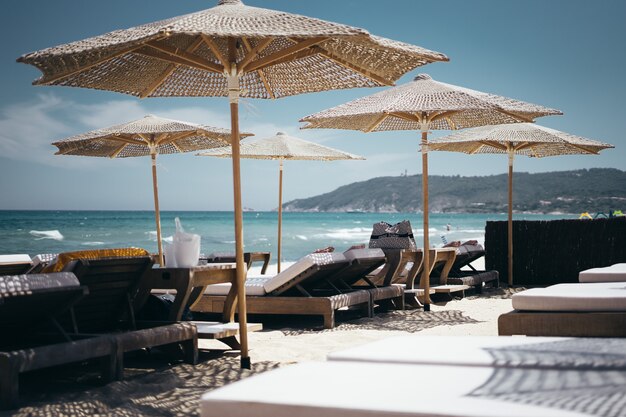 Selective wide shot of brown wooden loungers under parasols by the beach