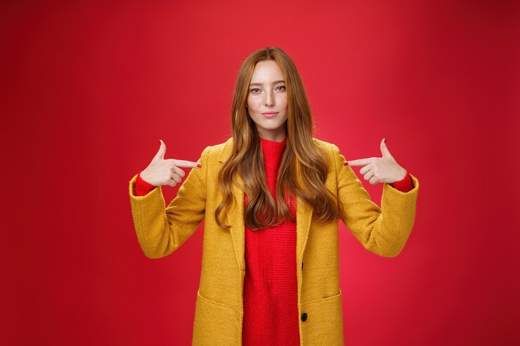 मुफ़्त फोटो self-assured assertive and optimsitic charming female entrepreneur with ginger hair in yellow coat pointing at herself proudly brag own success or willing to be candidate smiling confident.