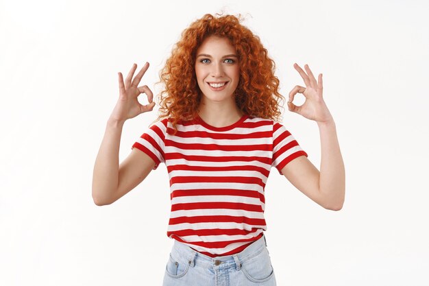 Self-assured assertive smiling attractive redhead curly girl show okay ok perfect gesture recommend excellent store smiling pleased approving good deal like everything, white wall