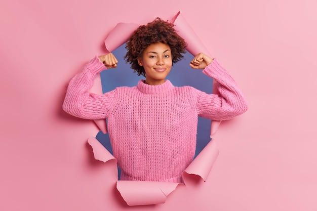 Self assured beautiful young afro american woman raises arms shows biceps being strong and powerful Free Photo