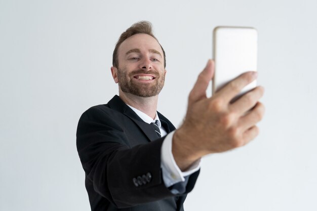 Self-assured business man posing and taking selfie photo on smartphone.